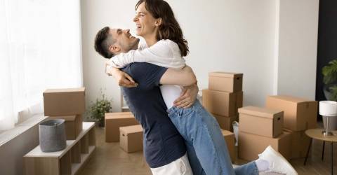 Eerste woning een droom die uitkomt jongen tilt een vrouw op in een woonkamer met allemaal dozen