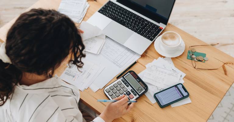Bovenaanzicht van een vrouw die thuis in de keuken werkt met financiële papieren